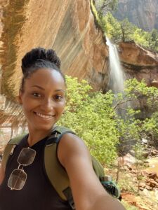 Taylor Curtis featured Care Champion, hiking, wearing her backpack, waterfall in background