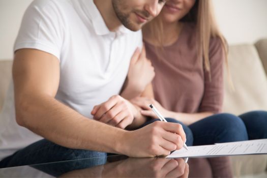 Adult couple man and woman sitting on couch signing paperwork on coffee table