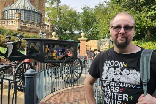 Client Daniel posing in front of the haunted mansion ride at Disneyland wearing a black shirt with characters, sunglasses and a gray backpack