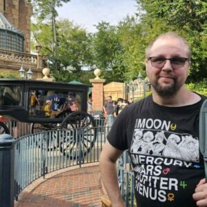 Client Daniel posing in front of the haunted mansion ride at Disneyland wearing a black shirt with characters, sunglasses and a gray backpack