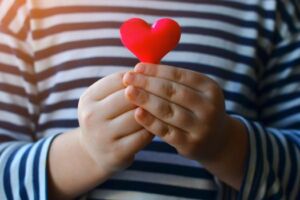 Young child in navy and white stripe long sleeve holding a red felt heart with both hands 