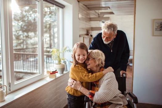 An older person and a young person are hugging in front of a window